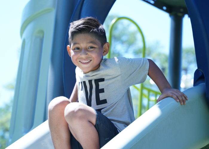 Young boy smiles before sliding down slide at playground. Credit: Ahmod Goins